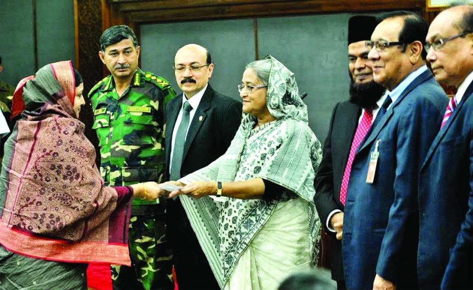Prime Minister Sheikh Hasina, in presence of A. Rouf Chowdhury, Chairman of Bank Asia and A.M. Nurul Islam, Vice Chairman at the Prime Minister's Office, is handing over a cheque of Tk.4.80 lakh to Mrs. Rashida Kabir Reba, widow of Major (late) Md. Humay