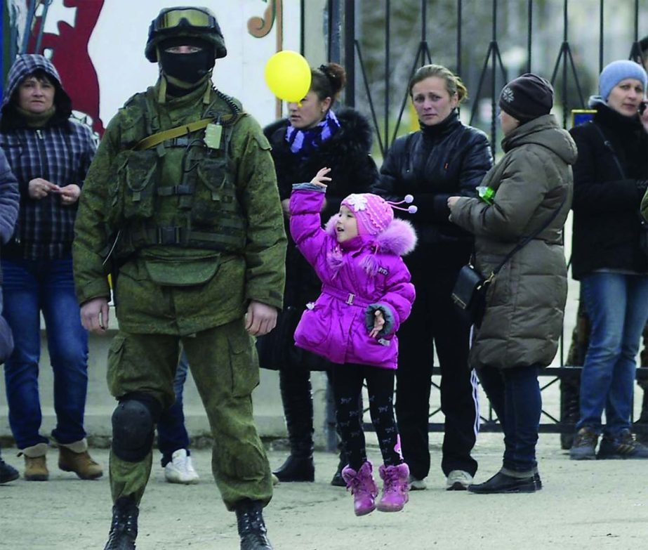 A girl plays with a balloon near an armed man, believed to be Russian servicemen, near the gates of a Ukrainian military unit in Crimea.
