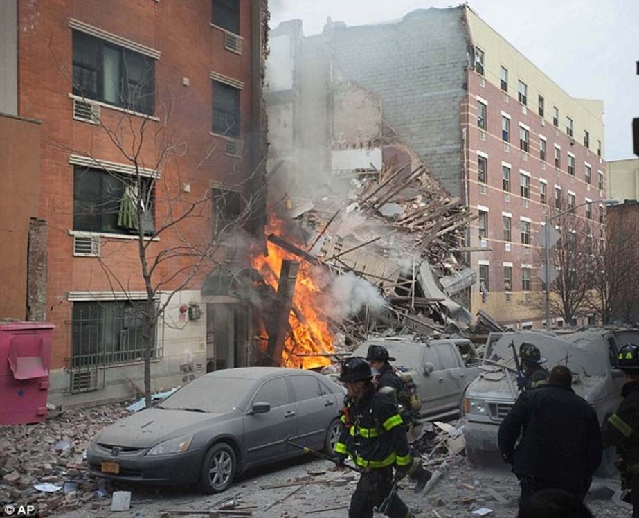 Firefighters work the scene of an explosion as flames leap up the towering heap of rubble.