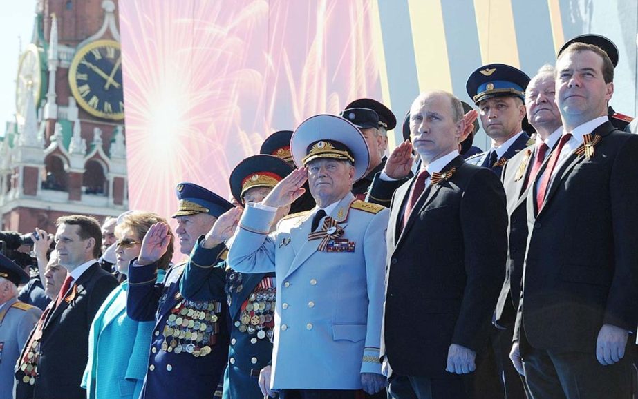 Putin and Prime Minister stand up alongside other senior Kremlin figures as troops march in front of them on Friday.