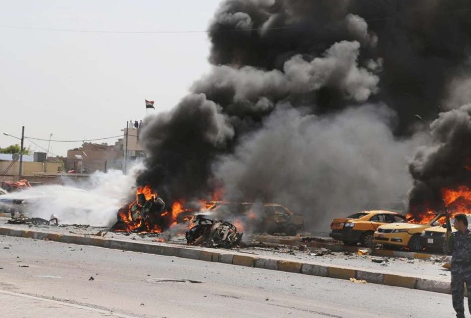 An Iraqi policeman looks at firefighters trying to extinguish burning vehicles moments after one in a series of bombs hit the Shiite stronghold of Sadr City, in Baghdad, Iraq, on Tuesday .