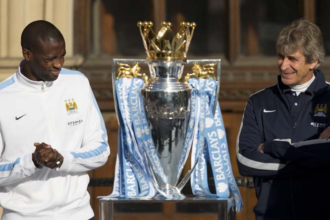 Manchester City's Yaya Toure (left) and manager Manuel Pellegrini stand by the trophy as the team celebrate in the city centre the day after they won the English Premier League title, Manchester, England on Monday.