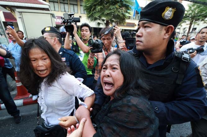 A friend, center, tries to help as an anti-coup protester, left, is detained by a Thai police officer during a protest on a street in Bangkok on Saturday.