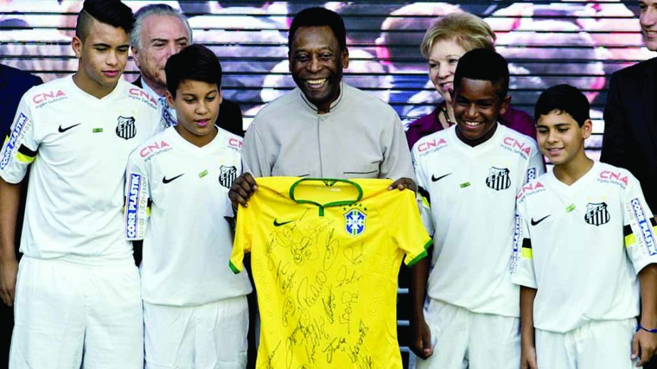 Brazilian football legend Edson Arantes do Nascimento (C) known as Pele, poses with young footballers after receiving a jersey of the Brazilian national team autographed by the players during the inauguration of the Pele Museum in Santos, some 70 km from