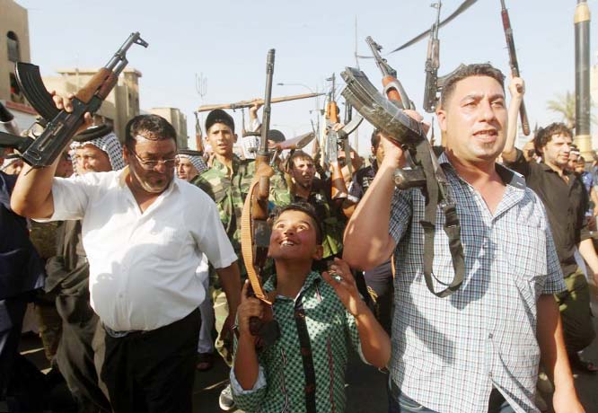 A Iraqi young boy and tribesmen hold up their weapons in the capital Baghdad today as they prepare for an ISIS attack
