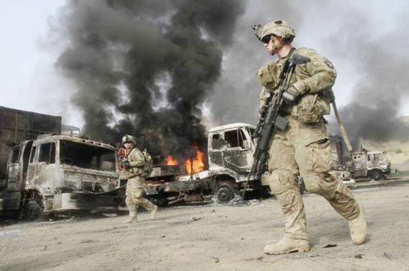NATO troops walk near burning NATO supply trucks after, what police officials say, was an attack by militants in the Torkham area near the Pakistani-Afghan in Nangarhar Province on Thursday.