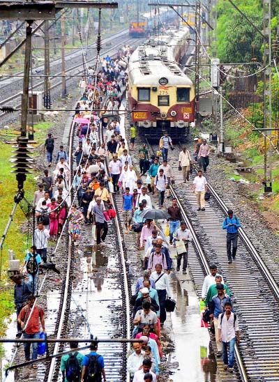 Commuters walk after local train stoped due to flooding at railway tracks during rain at Central Railway in Mumbai.