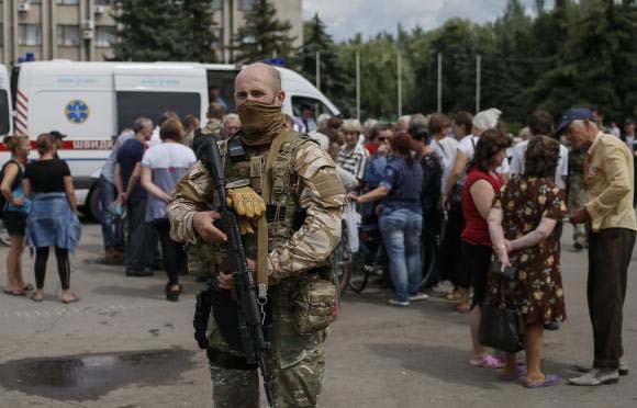 An armed man stands guard as people wait for humanitarian medical aid near the mayor's office in Slaviansk.