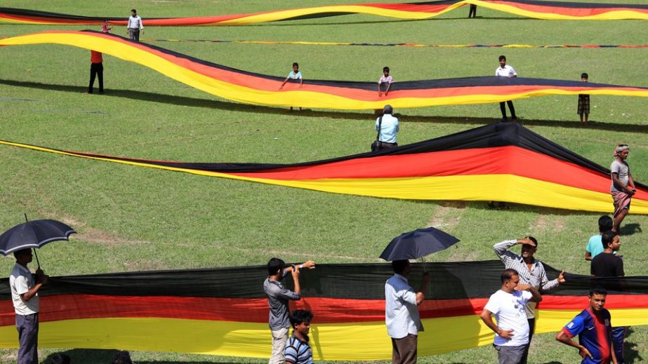 A BANGLADESHI FAN DOES IT : In this photograph taken on July 12, 2014 and released by the German Embassy in Dhaka, Bangladeshi residents stand alongside a large German flag displayed at a stadium in Magura. Germany has honoured a Bangladesh farmer and die