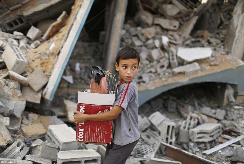 A Palestinian boy carries belongings as he walks past a house which police said was destroyed in an Israeli air strike, in Gaza City on Monday.