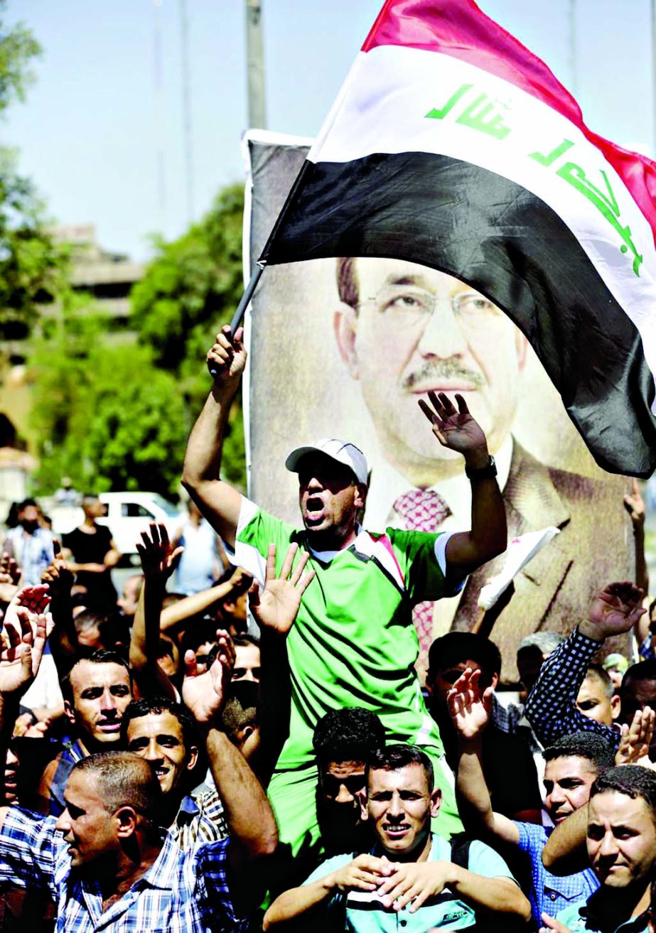 Iraqis chant pro-government slogans and wave national flags to show support for embattled Prime Minister Nouri al-Maliki during a demonstration in Baghdad on Monday.