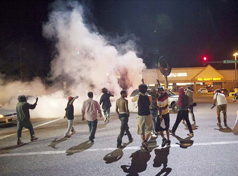 Smoke from a tire burnout rises over protestors on West Florissant Avenue during a tense demonstration.