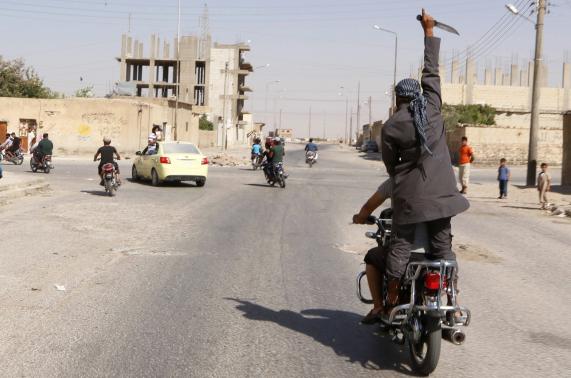 A man holds up a knife as he rides on the back of a motorcycle touring the streets of Tabqa city with others in celebration after Islamic State militants took over Tabqa air base, in nearby Raqqa city. Credit: REUTERSStringer