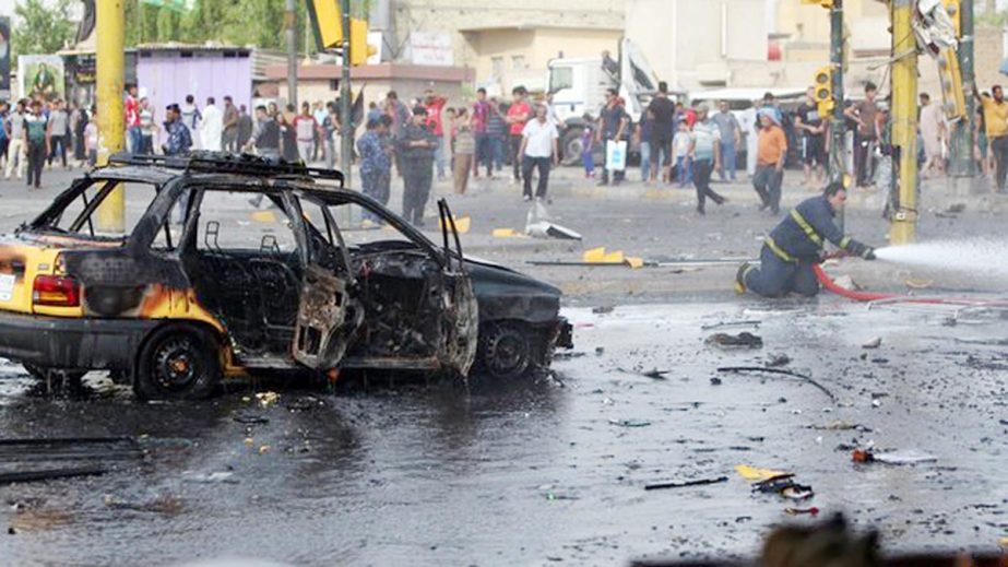 People gather as a member of the Iraqi emergency services extinguishes smoke at the site of a car bomb explosion in a commercial district of Baghdad.