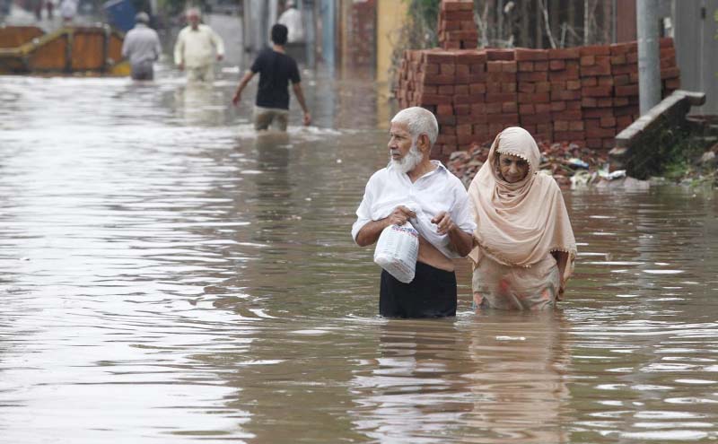 An elderly couple wading through a flooded road after heavy rains in Lahore.