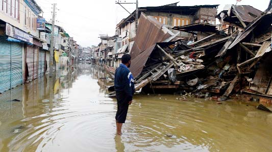 A Kashmiri resident stands in flood waters as he looks at a house that collapsed following the heavy rainfall that hit the area last week.