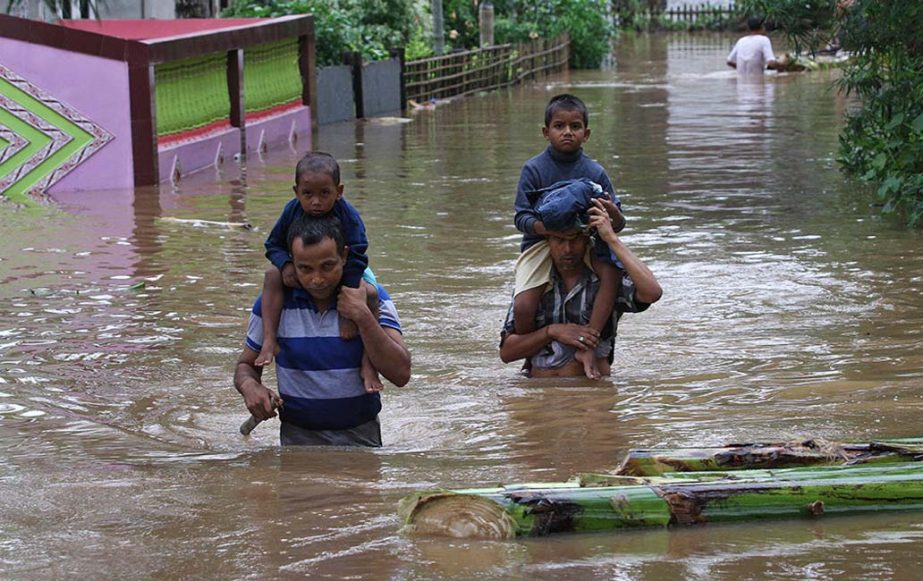 Indian villagers carry their children on their shoulders and wade through flood waters at the Chaygaon village in Kamrup district of northeastern Assam state, India.