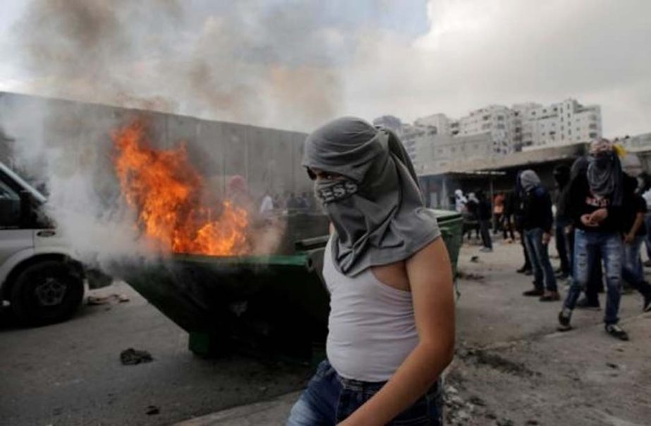 A Palestinian stone-thrower stands in front of garbage set ablaze during clashes with Israeli police on the outskirts of Jerusalem near Shuafat refugee camp.