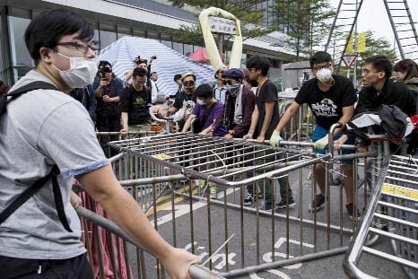 Masked pro-democracy protesters move a barricade further away from an office tower in accordance to a court injunction to clear up part of the protest site, after the arrival of bailiffs outside the government headquarters in Hong Kong