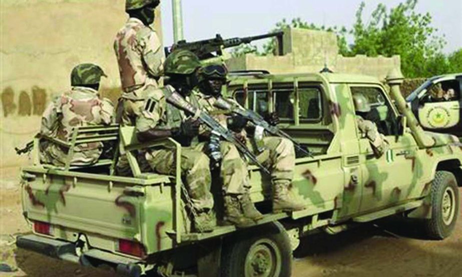 Nigerian soldiers hold their weapons as they sit on a military pick-up truck.