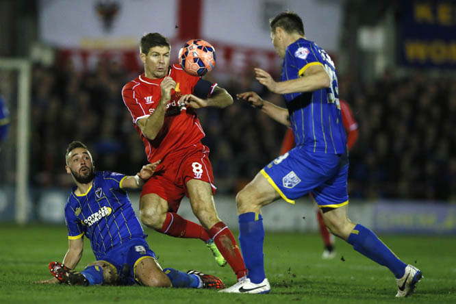 Liverpool's Steven Gerrard (centre) is challenged by AFC Wimbledon's Sammy Moore (right) and Jon Goodman (left) during their English FA Cup third round soccer match between AFC Wimbledon and Liverpool in Kingston, London on Monday.