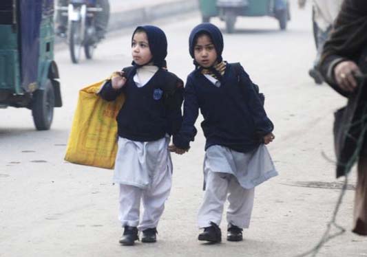 Girls carry their school bags as they walk along a road while heading to their school after it reopened in Peshawar on Monday.