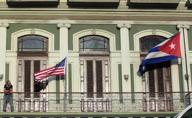 A man stands near the national flags of the US and Cuba (right) on the balcony of a hotel.