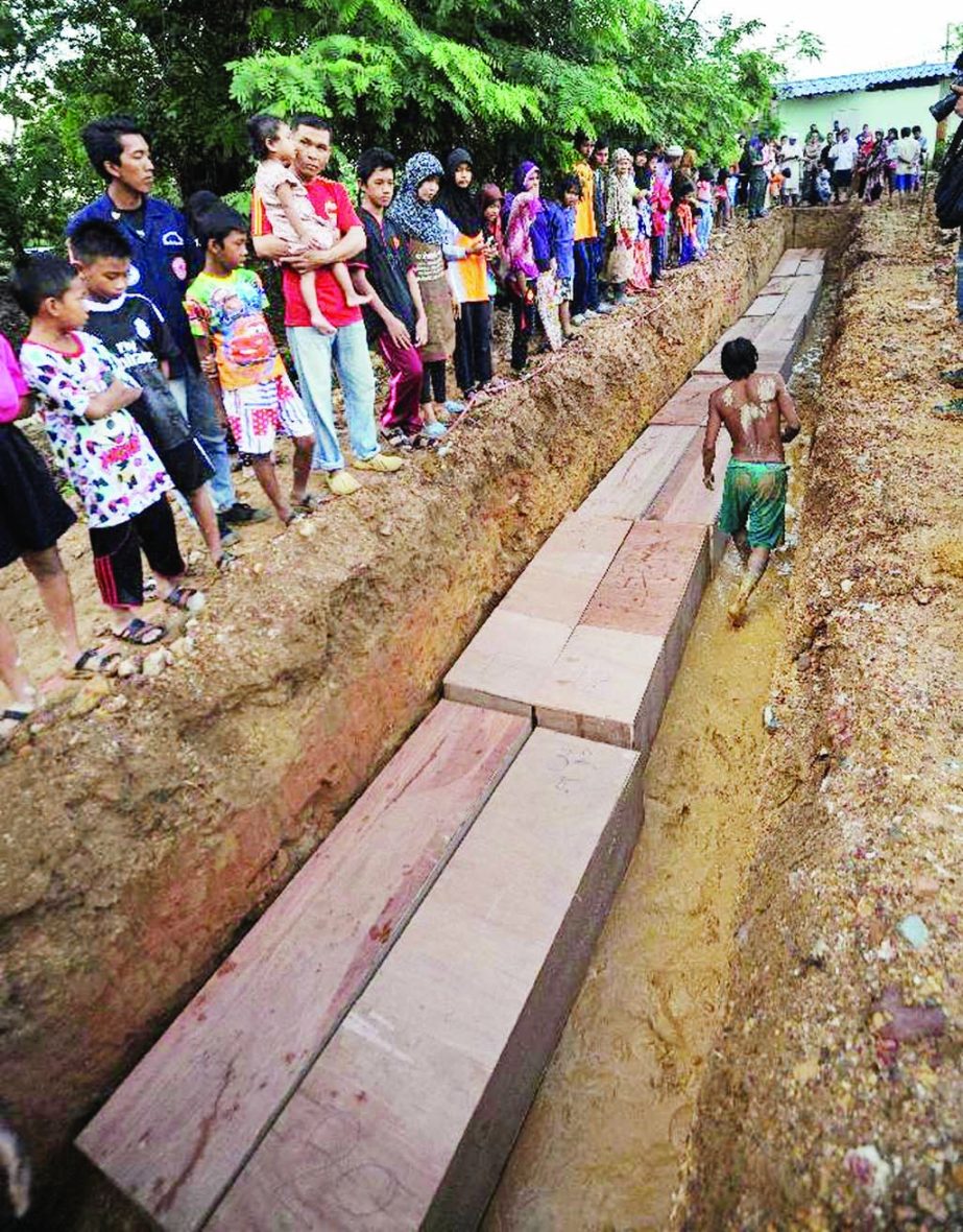 Residents watch as coffins containing the remains of migrants exhumed from a mass grave at an abandoned jungle camp in the Sadao district of Thailand's southern Songkhla province bordering Malaysia.