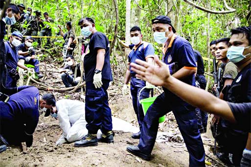 Policemen monitor as forensic experts dig out human remains near the abandoned human trafficking camp in the jungle close to the Thailand border at Bukit Wang Burma in northern Malaysia on Tuesday.