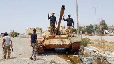 Members of the Libyan pro-government forces gesture as they stand on a tank in Benghazi, Libya.
