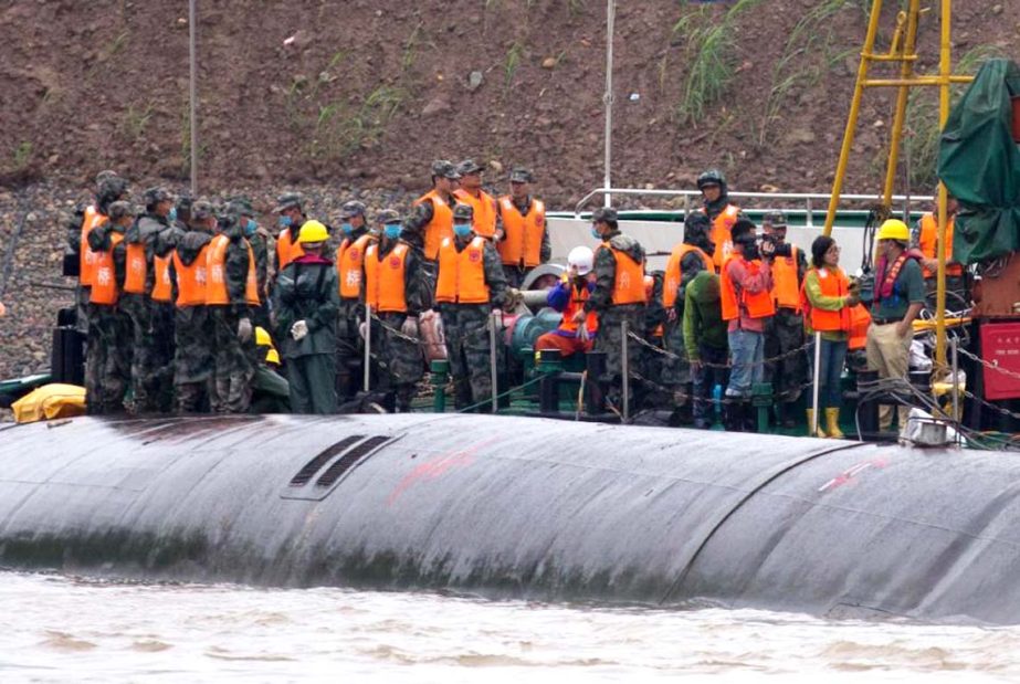 Chinese soldiers stand near a wrapped body as rescuers work on the capsized ship, center, on the Yangtze River in central China's Hubei province on Wednesday.