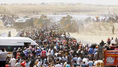 Turkish military use water cannon to stop Syrian refugees as they wait behind the border fences to cross into Turkey, near Akcakale in Sanliurfa province,.