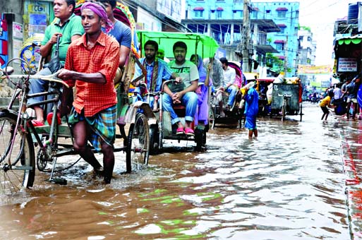 Residents of DND Dam areas of the capital using rickshaws to cross the road inundated by rain water on Sunday.