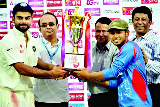 Bangladeshi Test cricket captain Mushfiqur Rahim (right) and visiting Indian skipper Virat Kohli (left) share the Test trophy at Khan Shaheb Osman Ali Stadium in Fatullah on Sunday.