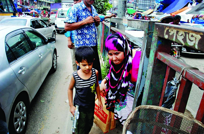 Disgusted with prolonged gridlock, a tiny-tot, holding toy gun in hand, escorts his mother to illegally cross the road defying barriers instead of using foot over bridge near New Market point on Monday. Photo: Sharif Khan