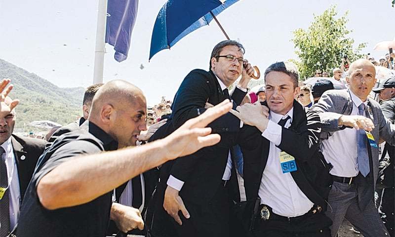 Bodyguards try to protect Serbian PM Vucic from stones hurled at him in Srebrenica.
