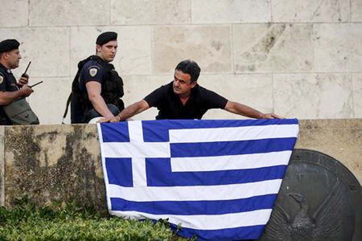 An anti-EU protester unfurls a Greek national flag next to riot police on the steps in front of the parliament building during a demonstration of about five hundred people in Athens, Greece .