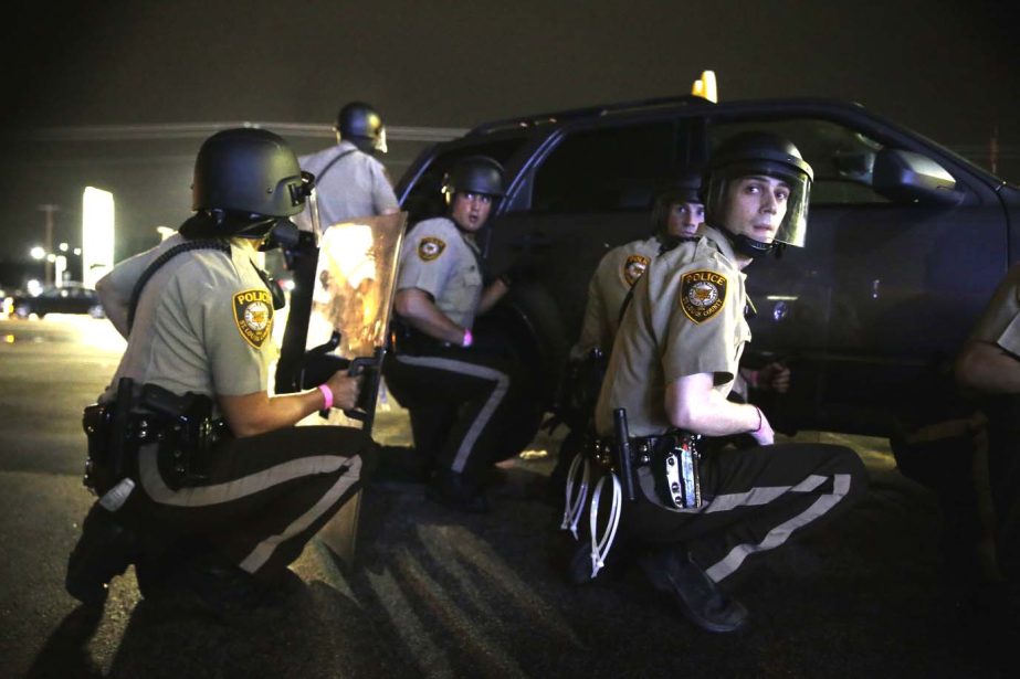 Police take cover behind a vehicle during a protest in Ferguson, Mo. on Sunday. The one-year anniversary of Michael Brown's death in Ferguson began with a march in his honor and ended with a protest that was interrupted by gunfire. AP