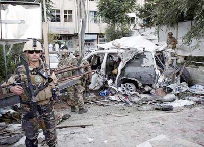 Afghan security personnel (L) keeps watch next to a damaged car belonging to foreigners, after a bomb blast in Kabul, Afghanistan on Saturday.