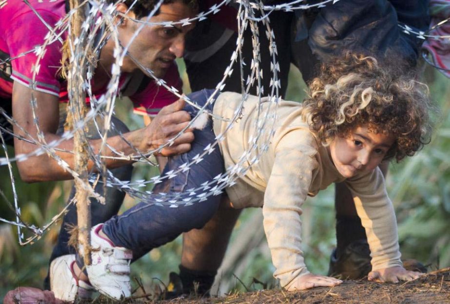 A refugee girl moves under barbed wire as she crosses from Serbia to Hungary, in Roszke on Thursday