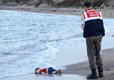 A Turkish police officer stands next to the body of a migrant child on the shores in Bodrum, southern Turkey on Wednesday after a boat carrying refugees sank while trying to reach the Greek island of Kos.