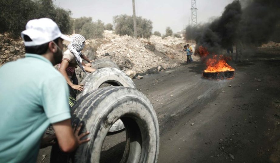 Palestinians roll tires in order to build a burning wall of tyres during clashes with Israeli army in the West Bank village of Kfar Qaddum.