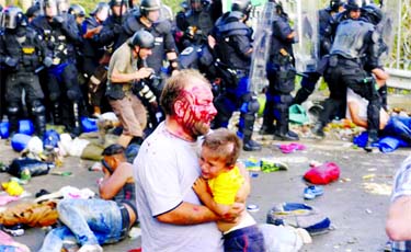 An injured migrant carries a child during clashes with Hungarian riot police at the border crossing with Serbia in Roszke, Hungary, on Wednesday. Internet photo