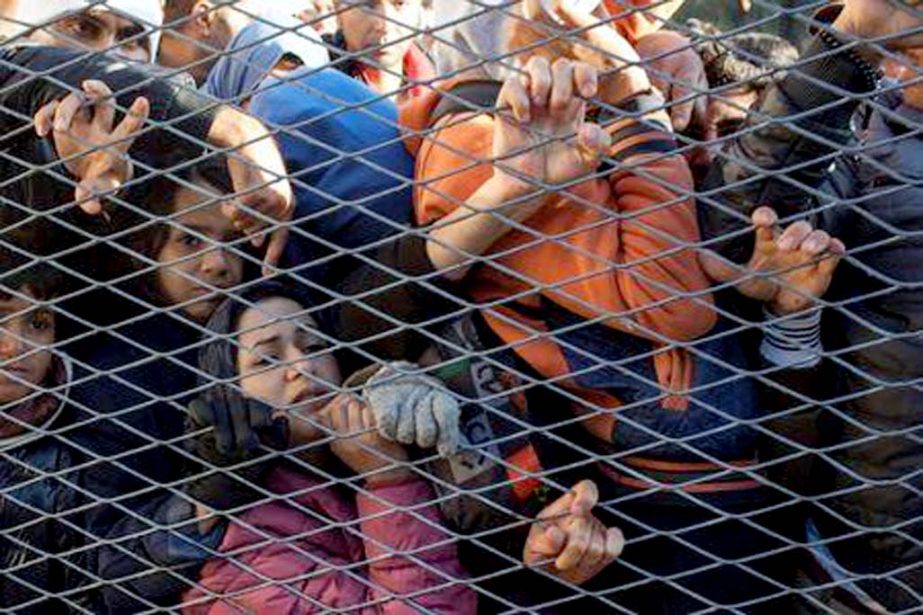 Migrants stand behind a gate as they wait to board buses inside a registration camp in Opatovac, Croatia on Wednesday.