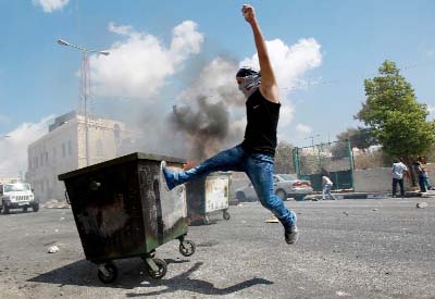 A masked Palestinian youth kicks a garbage container during clashes with Israeli security forces at the main entrance of the West Bank city of Bethlehem.