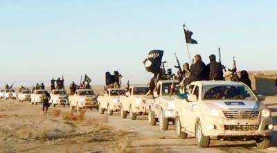 Islamic State group hold up their weapons and wave flags as they ride in a convoy, which includes multiple Toyota pickup trucks, through Raqqa city in Syria on a road leading to Iraq.