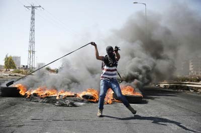 A Palestinian protester uses a slingshot to throw stones towards Israeli security forces during clashes in Beit El, near the West Bank city of Ramallah