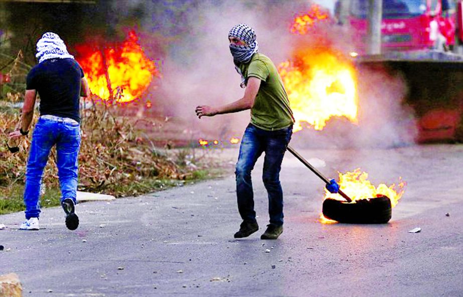 A Palestinian protester pulls a burning tyre behind him during clashes with Israeli security forces near West Bank.