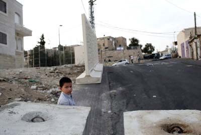 A Palestinian boy stands next to a new part of a wall put in place by Israeli officials to start to separate the Palestinian neighborhood of Jabel Mukaber from the Jewish settlement of Armon Hanatziv (background) in east Jerusalem.