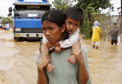 A woman carries her baby on her shoulder as they wade along a flooded highway in Sta Rosa, Nueva Ecija in northern Philippines October 19, 2015, after it was hit by Typhoon Koppu.